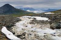 NORWAY, Troms, Lyngsalpan (Lyngen Alps). Melting snowdrift beside Kalddalen stream.