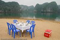 VIETNAM, Northeast, Halong Bay. Table set up for tourist lunch on a small beach amongst limestone karst towers.
