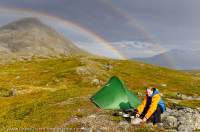 NORWAY, Troms, Lyngsalpan (Lyngen Alps). Rainbow over Lomvatnan lakes, with camp.