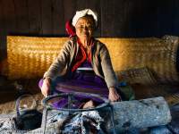 Old Palaung woman sitting at fire site within her traditional-style house, northern Shan Highlands.